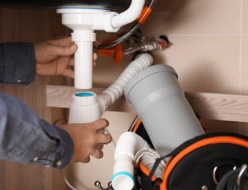 Professional male plumber replacing sink trap indoors